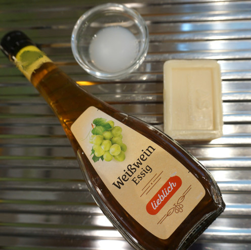 Auf einer Spüle liegen eine Flasche mit Essig, ein Schälchen mit Spülmittel und ein Stück Kernseife