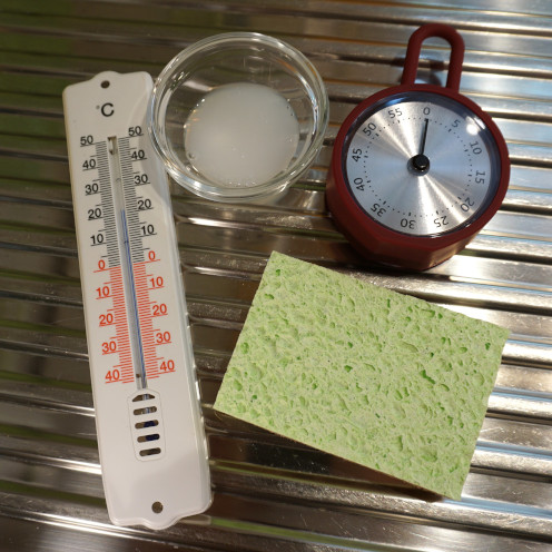 Auf einer Spüle liegen ein Thermometer, ein Schälchen mit Spülmittel, ein Kurzzeitwecker und ein Spülschwamm