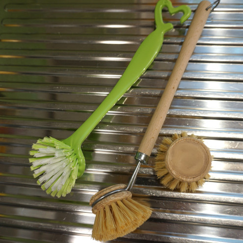 Auf einer Spüle liegen eine Spülbürste aus Plastik und eine Spülbürste aus Holz mit einer Bürste zum Wechseln