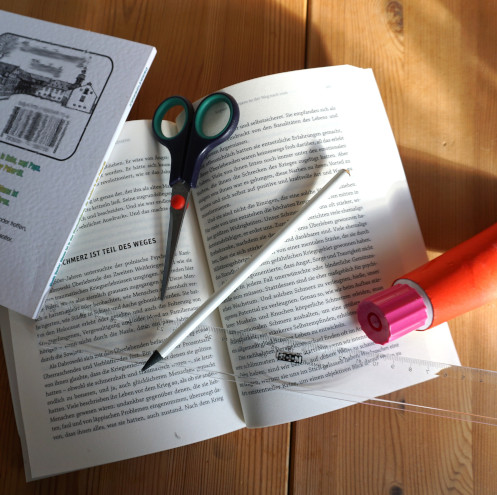 Aufgeschlagenes Buch mit Schere, Bleistift, Lineal und Kleber