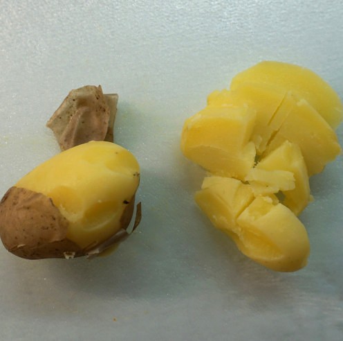 Zum Teil gepellte Kartoffeln und Kartofflscheiben auf einem Brett